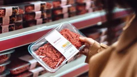 Getty Images A woman holds a packet of beef mince in a supermarket with rows of mince on shelves in the background
