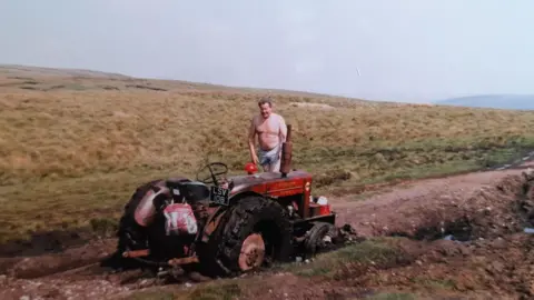 Dave Harrison Dave standing on top of a red tractor in a ditch.