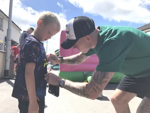 BBC James McClean signs a young fan's shirt at the street party