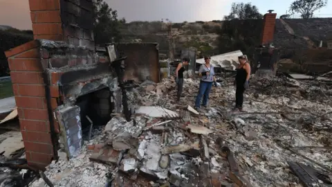 Getty Images Three women stand in the burnt out shell of a house in southern California following the wildfires.