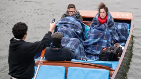 PA Media People wrap in blankets as they take a punt tour along the River Cam in Cambridge