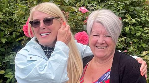Heather - with blonde hair and a light blue jacket - and Marian - with white hair and wearing a flowery dress and a black jumper - both smiling for the camera 