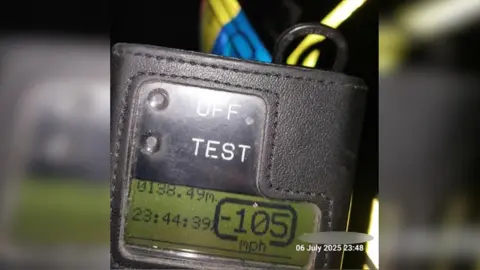 A police speeding device has a digital display that shows the time, which is 23:44:39, and a speed of 105mph.