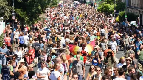 A large crowd of hundreds of people in the street during St Paul's Carnival on a sunny day.