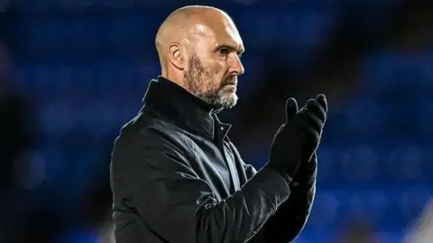 Getty Images Luke Williams, a man, wearing a black jacket and black gloves clapping his hands
