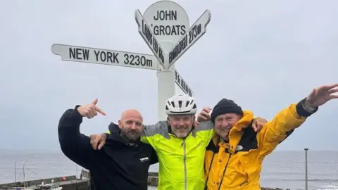 Exist Skatepark  Ric Cartwright, Mathew Pritchard and Paul Phillips posing in front of the John O'Groats sign, with the sea behind them. 