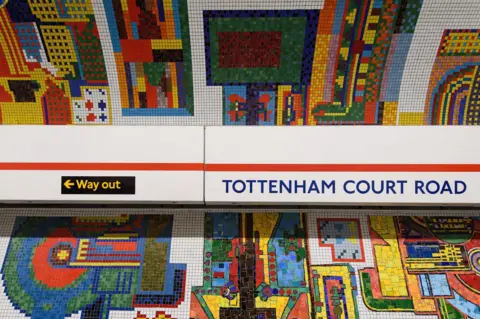 Getty Images Colourful, intricate mosaics, including patterns of cubes and circles on the walls of an underground train station. A sign reads "Tottenham Court Road", another reads "Way Out".