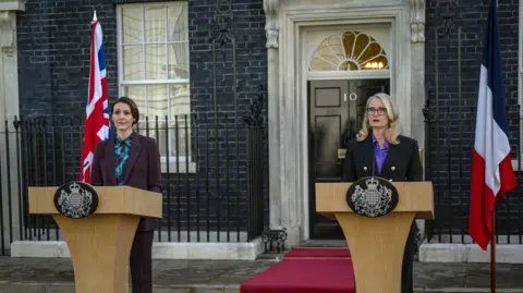 Netflix Suranne Jones and Julie Delpy in character standing outside no10 downing street in front of lecterns 