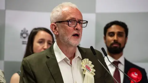 Jeremy Corbyn speaks during an acceptance speech with Labour's Praful Nargund in the background
