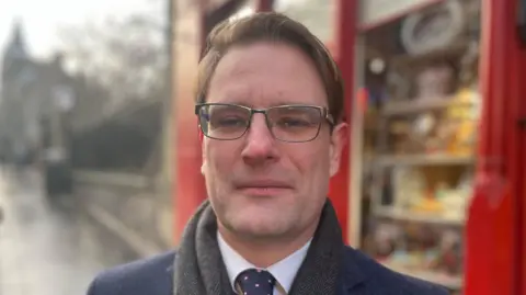 Ewan MacDonald-Russell from Scottish Retail Consortium has short brown hair and wears glasses and a dark navy suit and tie