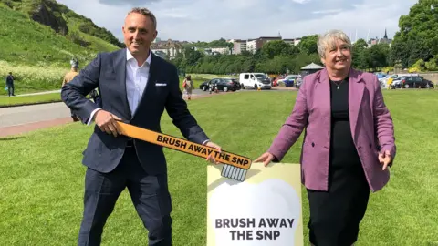 PA Media Alex-Cole Hamilton holding a big toothbrush with "brush away the SNP" on it