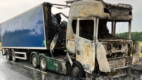 The burnt-out remains of the lorry with the charred cab and part of the blue trailer destroyed