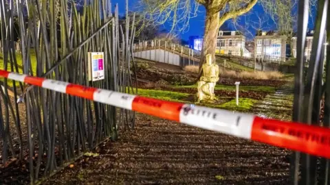 Red and white police tape crosses a gate before a statue in front of a tree outside Drents Museum in Assen, the Netherlands