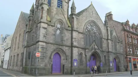 BBC A stone-built church on the corner of a street with bright purple doors.