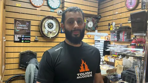 Man with full beard wearing a Tough Mudder t-shirt at a watch repair shop