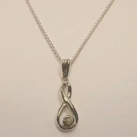 Paige Hawkins A silver necklace on a cream background. The necklace has a pendant shaped like a figure of eight, with a larger lower loop and a small pearl resting in the lower loop.