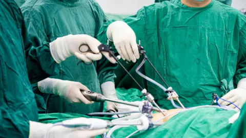 A group of doctors wearing green scrubs preparing to operate on a patient