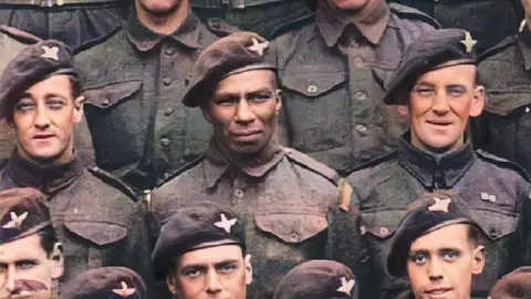 BBC members of the Parachute Regiment pose in uniform and beret. The original black and white picture has been colorized. Sidney Cornell is flanked by four white paratroopers in this cropped image of part of the group.