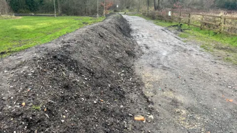 High pile of dirt on the side of a muddy pavement.