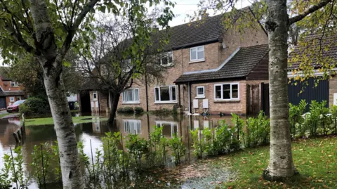 John Devine/BBC Two semi-detached houses on Hansell Road, Brampton, with water lapping their front doors. The house on the left was breached and the home was evacuated. The right hand one did not have water in because the resident said it was "half a brick higher".