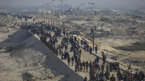 EPA Palestinians make their way along the coastal road in northern Gaza, past the ruins of destroyed buildings (2 February 2025)