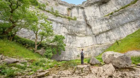 Getty Images/Nick Brundle Photography A person looks up at Malham Cove, Yorkshire Dales National Park.