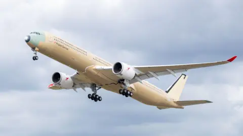 A large cream-coloured plane flies upwards against a cloudy blue sky.