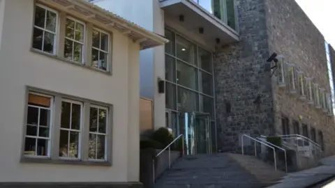 BBC The exterior of the grey walled court with steps leading up to the glass door