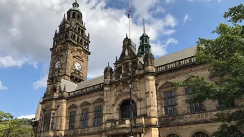 Sheffield Town Hall - a large historic building with turrets and a clock tower. There is a balcony above the entrance at the front of the building and a Union Flag flying on a pole.