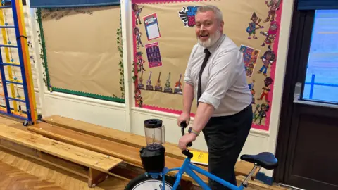 Colin Richardson sitting on a bicycle in a schoolroom 