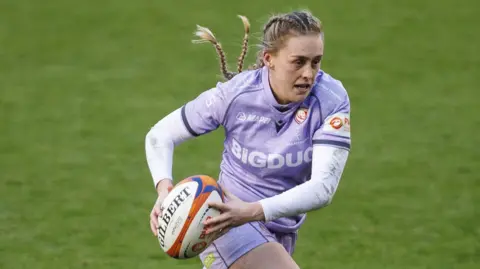 Gloucester-Hartpury centre Hannah Dallavalle wearing a purple Rugby shirt and carrying the ball during a Premiership Rugby game. 