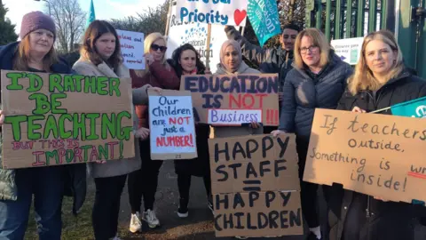 NEU Staff pose for a picture holding placards and homemade signs. 