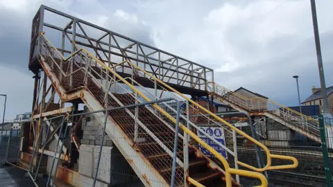 A rusty metal bridge with yellow handrails. 