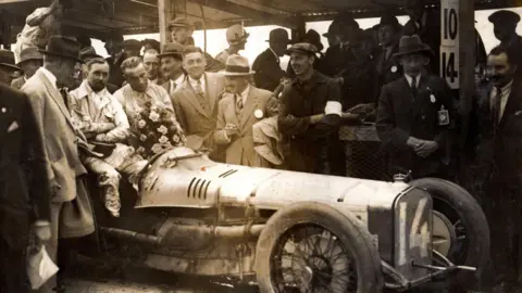 Brooklands Museum A sepia photo of men around a old racing car. 