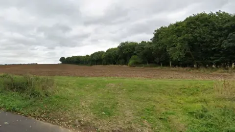 Google A ploughed field with a grass verge, and a tree-lined border on the right side.