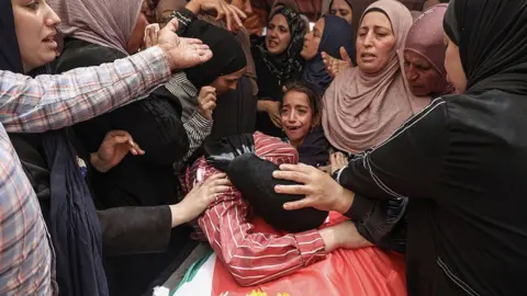 AFP Relatives mourn over the body of 17-year-old Palestinian Fadi al-Nassan during his funeral in the village of al-Mughayyir, in the occupied West Bank (18 July 2026)