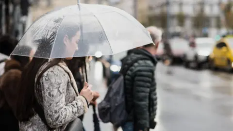 Getty Images Woman holds umbrella while walking across the street on a grey rainy day