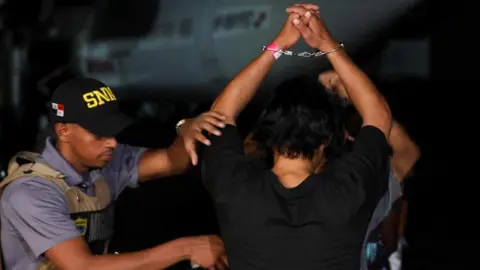 A Panamanian migration officer checks Colombian migrants who were detained after crossing into Panama irregularly through the dangerous Darien Gap, while they are handcuffed before boarding the first U.S. funded repatriation flight, at Tocumen International Airport, in Panama City, Panama August 20, 2024.