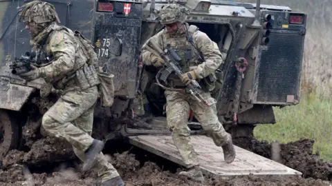 Getty Images Soldiers carrying rifles rush out of a vehicle as the British Army demonstrate the latest and future technology used on operations across the globe on Salisbury plain training area