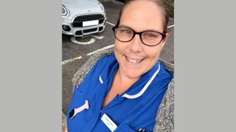 Sarah Jayne Crook, a woman in her 30s, is wearing a nurse's uniform. She is smiling and has dark hair. 