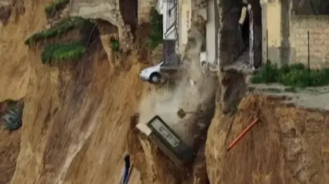 A car teetering on the edge of a drop after a landslide