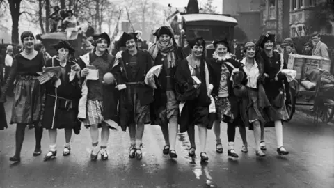 A black and white picture of women students from Reading University walking down a road in fancy dress.
