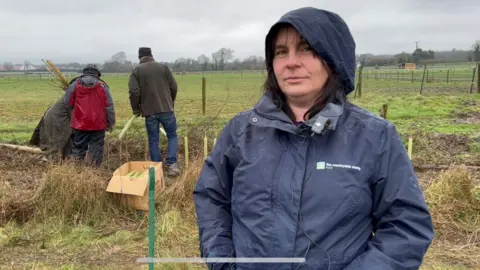 Chrissie Reidy/BBC Andrea Griffiths, director at the Campaign to Protect Rural England in Kent. Andrea is wearing a navy coat with the hood up. She has brown hair. Volunteers can be seen in the background.