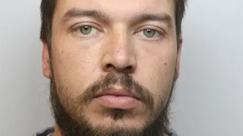 Cheshire Constabulary A police mugshot of Joshua Eldred, who has green eyes, a dark brown hair and a wispy, unkempt beard and moustache