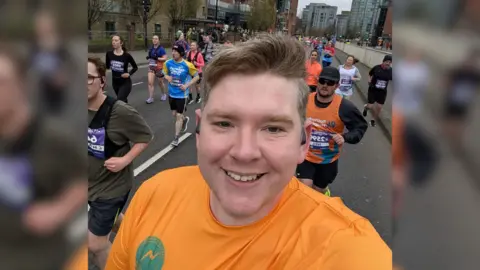 Scott Storey, a man in his late 30s, smiling whilst running alongside other participants in the Sheffield Half Marathon.