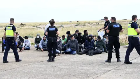 STEVE FINN Migrants waiting with police