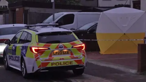 PA Media Image showing a police car and a police tent at a property on First Avenue in Dagenham