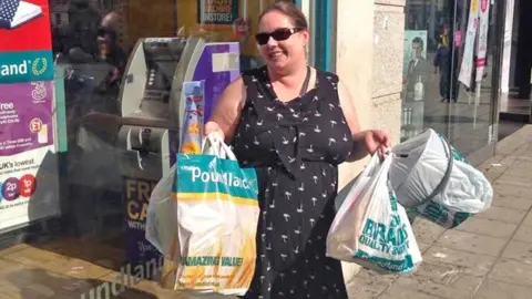 Sharon Carroll is pictured outside a Poundland holding many full shopping bags and smiling