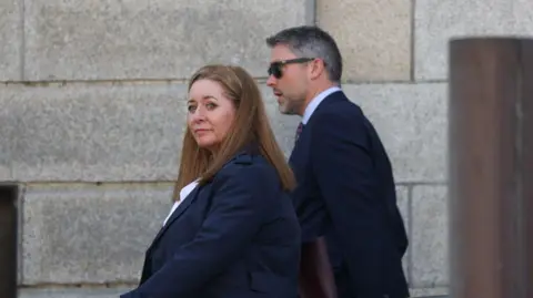 PA Media BBC Spotlight reporter Jennifer O'Leary walking outside the High Court in Dublin at an earlier hearing with BBC Northern Ireland Director Adam Smyth. Ms O'Leary has long, straight auburn hair and is wearing a navy overcoat and a white top. Mr Smyth has short, greying dark hair and a beard. He is wearing a navy suit and sunglasses.
