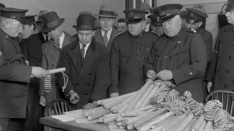 Fox Photos/Getty Images Special constables are issued with truncheons during the General Strike. A pile of wooden truncheons are on a table. Some of the men pictured are in uniform.